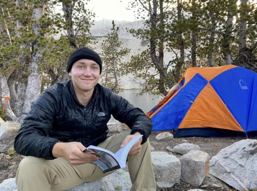 Jack Johnson '15 camping, reading a book, next to a tent